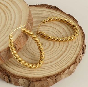 Detailed view of gold twisted oval hoop earrings displayed on natural wooden slices