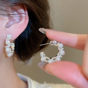 Detailed close-up of C-shaped silver earrings with pearls and shimmering pavé zircons