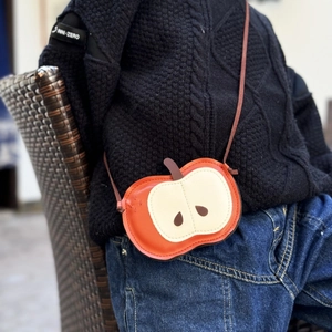 Detail of red apple shaped kids crossbody bag with soft litchi texture and cord strap