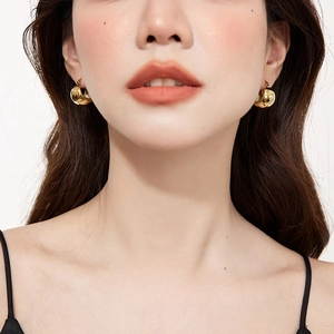 Close-up of polished 18K gold C-shaped chunky hoop earrings worn on model's ear