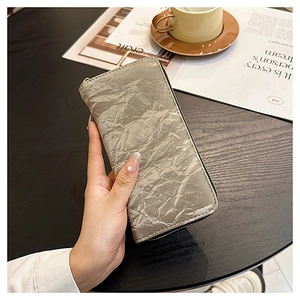 Silver wrinkled texture long wallet held over a wooden table with aesthetic coffee decor