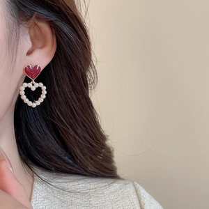 Detail of red enamel heart and pearl drop earrings on model in warm studio lighting