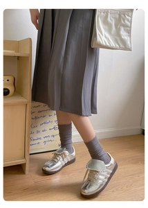 Detail of grey knitted calf socks paired with metallic sneakers and a pleated skirt