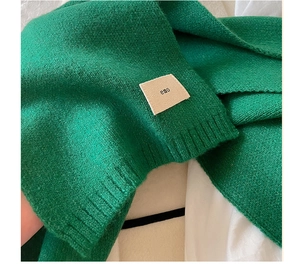 Detail of green knitted scarf featuring a ribbed edge and small embroidered emo label