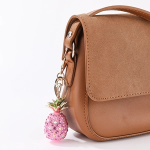 Sparkling pink pineapple keychain with crystals hanging on a premium leather handbag