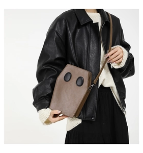 Detail shot of coffin-shaped brown crossbody bag with black patches and silver hardware