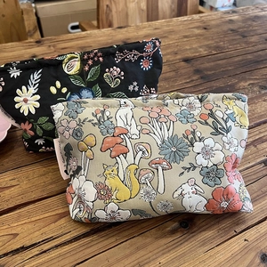 Large floral and forest animal canvas makeup bags on a wooden table for travel storage