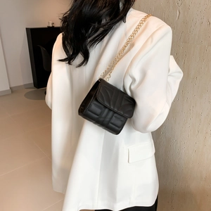 Classic black quilted square crossbody bag with gold chain strap worn with white suit