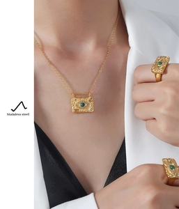 Detail of gold evil eye necklace and rings with green stones worn with a white blazer