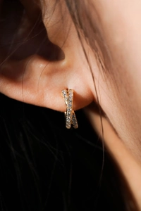 Close-up of golden twisted hoop earring with double-row crystals worn on ear