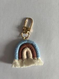 Macro detail of hand-woven rainbow charm with cotton fringes and gold metal clasp