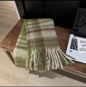 Detail of a thick plaid scarf with long tassels on a table next to a laptop