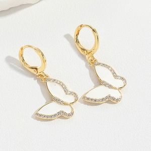 Detailed macro view of gold-tone dragonfly earrings with white enamel and micro-pavé crystals