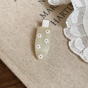 Close-up of cream resin water drop hair clip with white floral motifs and silver metal grip