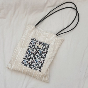 Detail of white lace texture tote bag featuring a butterfly patch and black straps