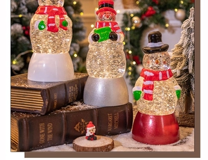 Drei dekorative, beleuchtete Schneemann-Schneekugeln auf alten Büchern für Weihnachten
