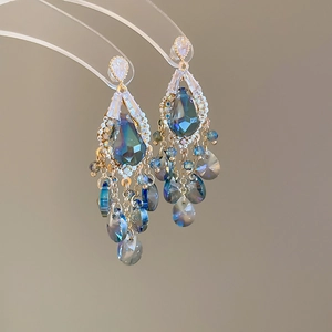 Macro detail of blue glass teardrop tassel earrings with intricate golden metal frames