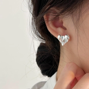 Close-up of irregular silver heart stud earring with liquid lava texture on model