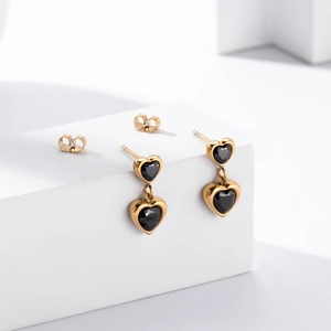 Boucles d'oreilles cœur dorées avec pierres noires sur un support minimaliste