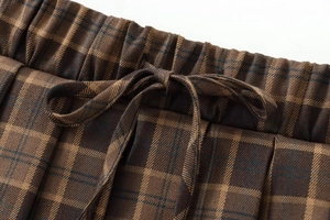 Detail of elastic waistband with drawstring bow on brown plaid pleated mini skirt