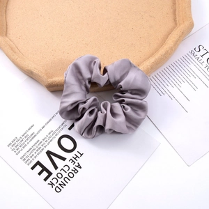 Detail of a large grey satin silk hair scrunchie placed on a minimalist cork tray