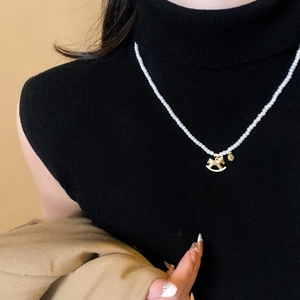 Detail of white pearl necklace with golden rocking horse pendant on black knitwear