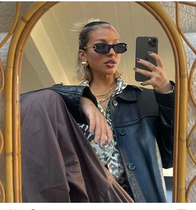 Detail of retro oval black sunglasses paired with gold layered necklaces and leather jacket