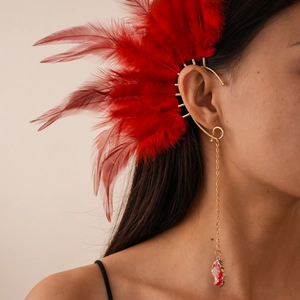 Λεπτομέρεια χρυσού ear cuff με κόκκινα φτερά και μακρύ κρυστάλλινο κρεμαστό κόσμημα