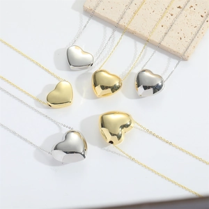 Minimalist polished gold and silver heart pendant necklace on a modern stone backdrop