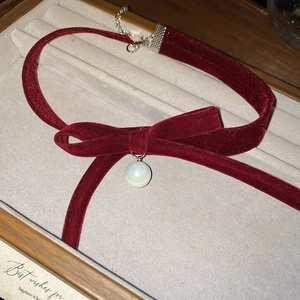 Detail shot of vintage red velvet bow necklace with iridescent pearl on gray jewelry box