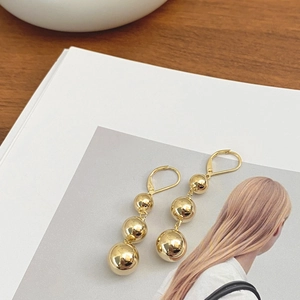 Modern gold lever-back earrings featuring a vertical triple ball drop design on a magazine
