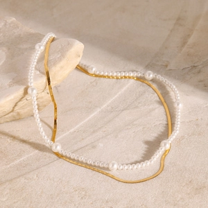 Detail of layered gold snake chain and white pearl necklace on textured stone background