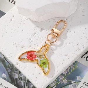 Detailed close-up of a whale tail resin keychain with real dried flowers and gold metal trim