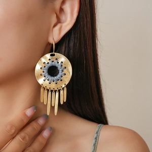 Detail of gold geometric hollow hoop earring with grey woven cord and tassel charms