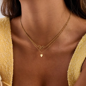 Close-up of double layer gold stainless steel necklace with bow and heart pendants