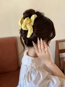 Detail of yellow pleated fabric hair claw clip on a dark brown bun for women