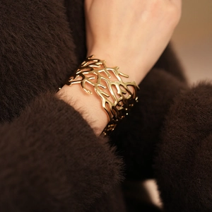 Detailed close-up of golden hollow coral textured cuff bracelet on model sleeve