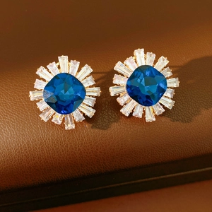 Macro detail of vintage floral stud earrings with blue square gemstone and gold finish
