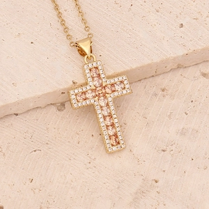 Detailed close-up of a gold cross necklace with champagne zircons on a beige stone base