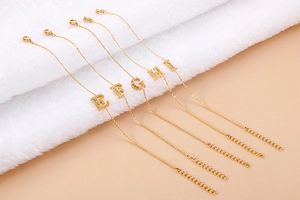 Detail of gold letter bracelets E to I with rhinestones on white fur and pink background