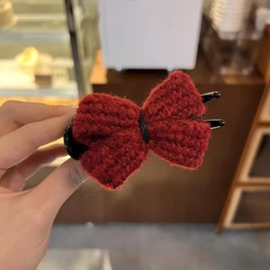 Detail of a red knitted bow hair claw clip held in hand with soft natural lighting