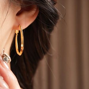 Detailed close-up of textured golden hoop earring featuring a minimalist twisted design