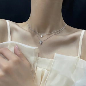 Detail of silver double-layered necklace featuring a zircon cross pendant on a female model