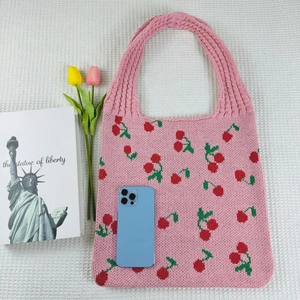 Flat lay of pink knitted tote bag with red cherry patterns and decorative accessories