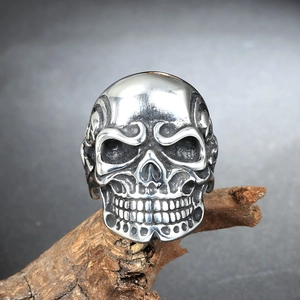 Macro shot of silver skull ring with detailed engravings on a dark rustic wood stand
