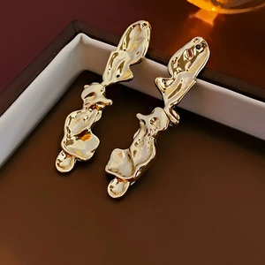 Close-up of irregular molten gold lava earrings on a brown luxury jewelry box