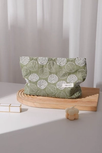 Close-up of floral embroidery on green linen makeup bag with woven brand label