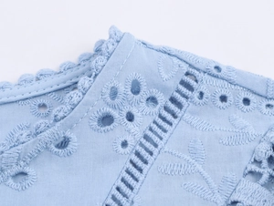 Dettaglio ravvicinato di ricamo e finiture traforate su camicia in azzurro chiaro