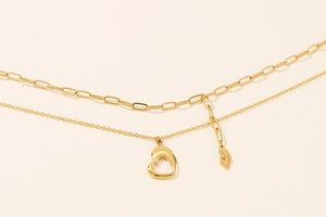 Close-up of double-layer gold necklace featuring a paperclip chain and heart pendant