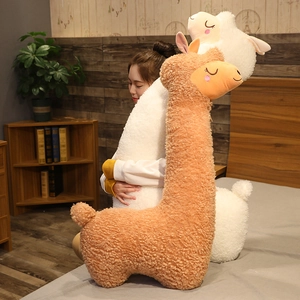 Soft cartoon alpaca plush toy in a cozy bedroom lifestyle setting held by a model